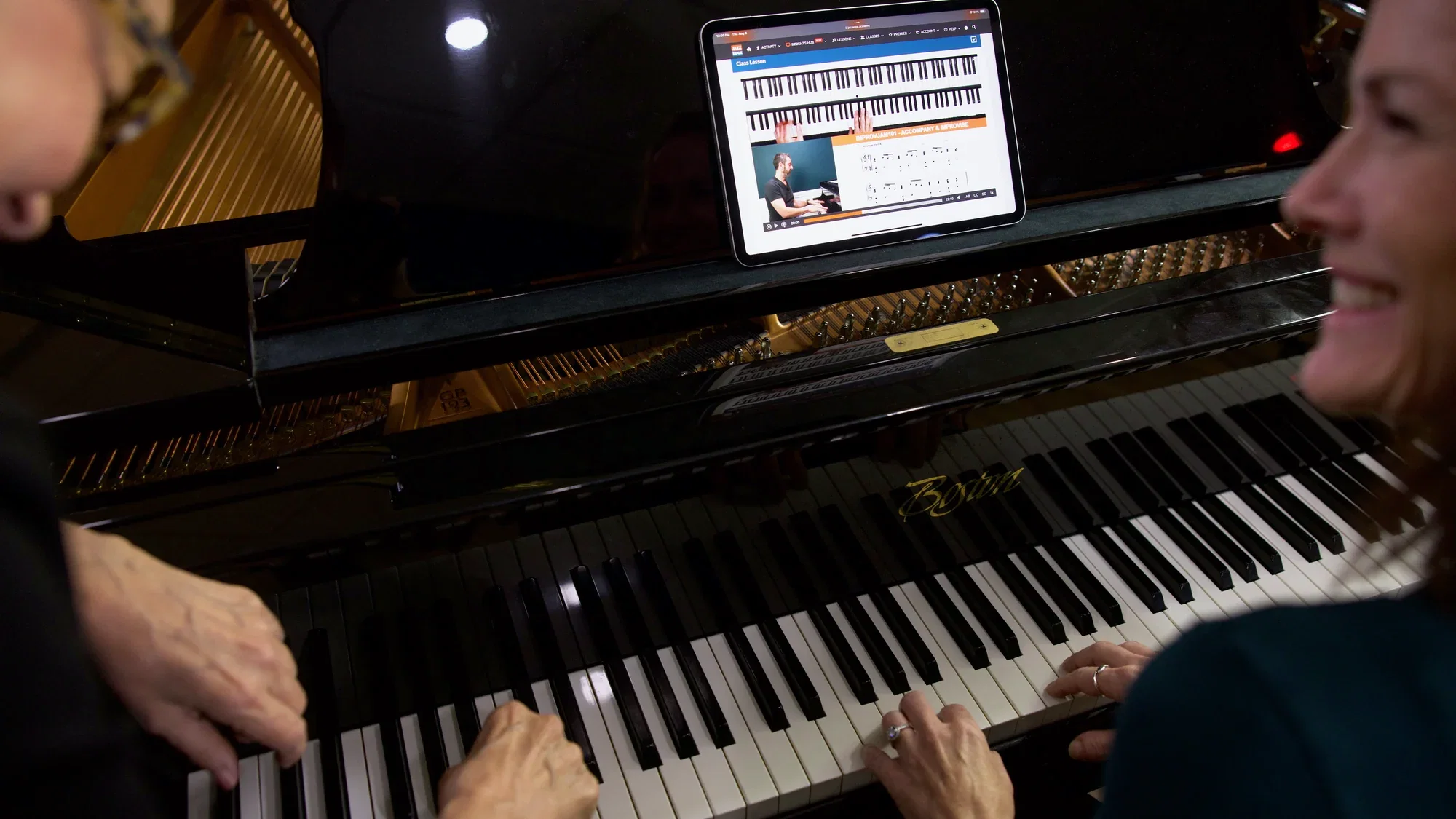 Two people playing a grand piano together with a Jazzedge lesson open on a tablet