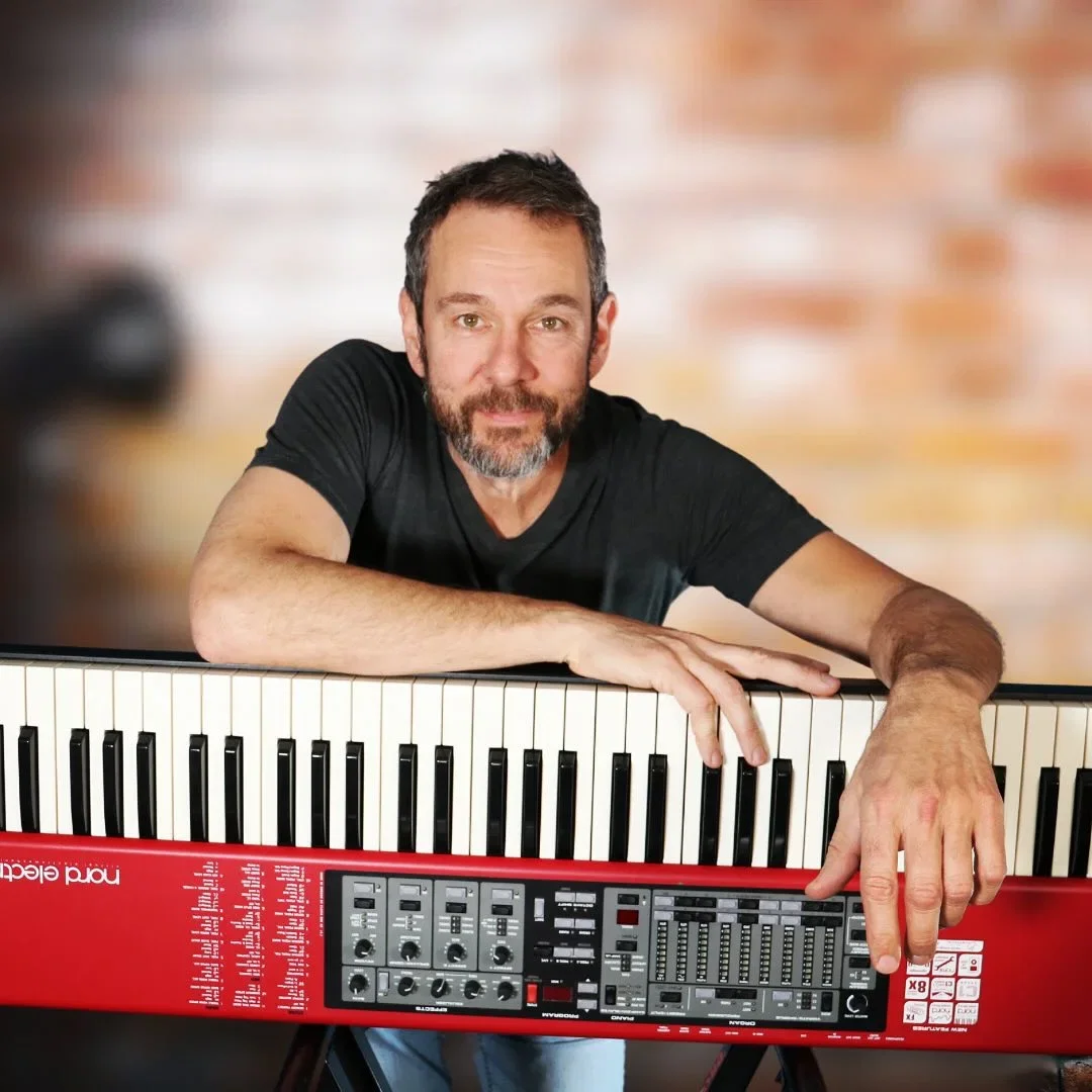 Willie Myette leaning on a Nord Electro stage piano, looking toward the camera